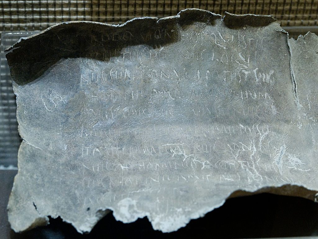 Rzymska ołowiana tabliczka z zaklęciem rzuconym na kobietę o imieniu Rhodine. W tekście zaklęcia przywoływany jest bóg zaświatów Dis Pater, utożsamiany z Plutonem. Połowa I wieku p.n.e. Znaleziona w grobie w pobliżu Via Latina w okolicy Rzymu. Tabliczki zaklęć z południowej Italii różniły się od tej jedynie językiem tekstu i alfabetem, w jakim go zapisano.